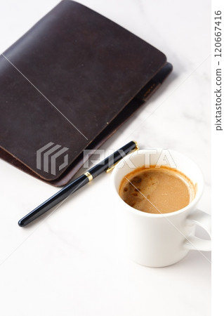Image of a man working at his desk with a brown leather organizer while drinking a cafe latte, a coffee with milk 120667416