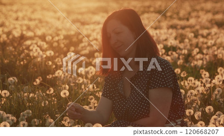 Beautiful Brunette Woman Blowing Dandelion On A Summer Field. Young Beautiful Girl With Long Hair Blows Dandelion. Slow motion. 120668207