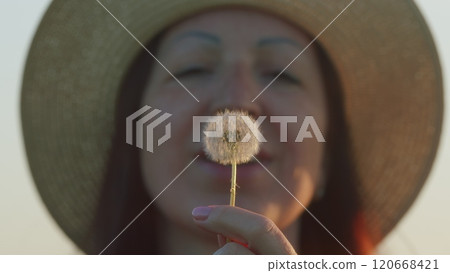 Portrait Of A Beautiful Brunette Female Blowing On Ripened Dandelion. Adorable Smiling Woman Blowing On Dandelion. Close Up. 120668421