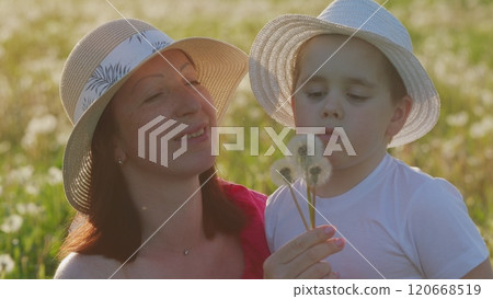Young Woman And Little Boy Blow On A Dandelions. Beautiful Mother And Cute Little Boy Blowing Together Dandelion Seeds. Moves slowly. Young Woman And Little Boy Blow On A Dandelions. Beautiful Mother And Cute Little Boy Blowing Together Dandelion Seeds. Moves slowly. 120668519