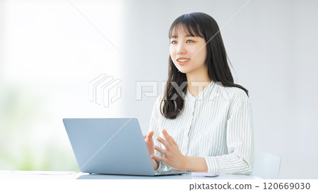 Smiling woman/businesswoman talking while using a computer Smiling woman/businesswoman talking while using a computer 120669030