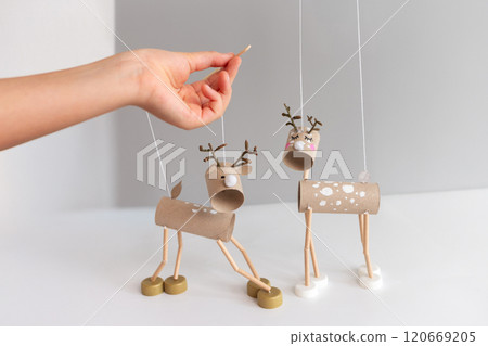 Festive DIY reindeer puppets made from cardboard tubes and bottle caps held by hand with wooden stick. Minimalist Christmas craft 120669205