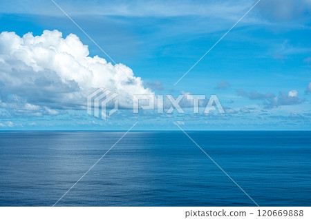 Serene ocean view with clear blue sky and large white clouds, calm water surface reflecting sunlight, peaceful seascape horizon, tranquil nature scene, beautiful weather, scenic coastal landscape 120669888