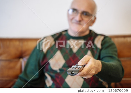 Elderly man holding TV remote control at home. Grandfather watching TV in living room Elderly man holding TV remote control at home. Grandfather watching TV in living room 120670009
