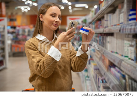Woman shopping for skincare products in a store while checking her phone for information Woman shopping for skincare products in a store while checking her phone for information 120670073
