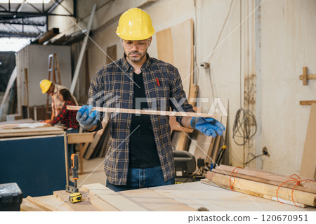Carpenter man holding piece of wood surrounded by other wood pieces, showcasing craftsmanship and happiness at work in a furniture factory. Ideal for woodworking and craftsmanship concepts. Labor day 120670951