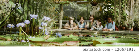 Wide shot of young female botanist showing aquatic plants growing in botanical garden greenhouse to group of teenagers, header for website Wide shot of young female botanist showing aquatic plants growing in botanical garden greenhouse to group of teenagers, header for website 120671913