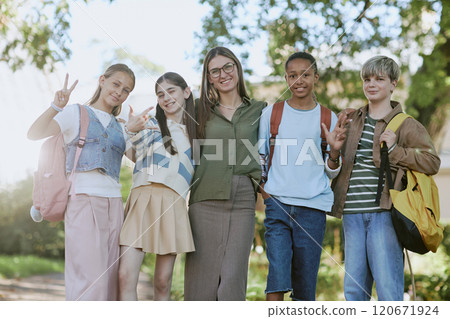 Low angle of cheerful young female tour guide and group of teen students posing for camera in botanical garden 120671924