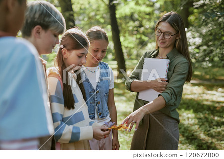Young Biology teacher telling about flower and leaves her students collected in botanical garden 120672000