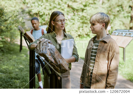 Young female botanical garden worker showing petrified wood while conducting tour for teen students 120672004