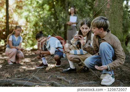 Group of teen boys and girls having fun picking up pine cones from ground in botanical garden during educational tour 120672007