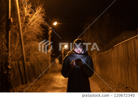 Couple holding hands while walking on a quiet road at night, illuminated by a streetlight, surrounded by bare trees and a serene atmosphere. Couple holding hands while walking on a quiet road at night, illuminated by a streetlight, surrounded by bare trees and a serene atmosphere. 120672340
