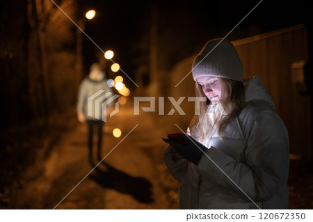 Couple holding hands while walking on a quiet road at night, illuminated by a streetlight, surrounded by bare trees and a serene atmosphere. 120672350