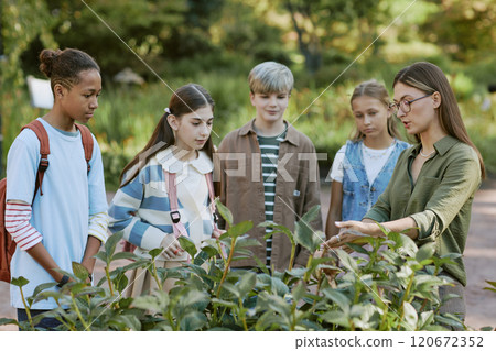 Young professional botanist working in botanical garden demonstrating plant to group of teen students 120672352