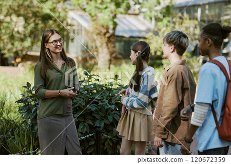 Medium long shot of young female teacher of Biology conducting class for kids in local botanical garden 120672359