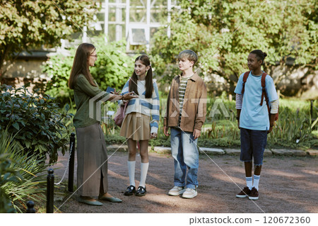Young female tour guide greeting group of diverse teenagers in botanical garden, wide shot 120672360