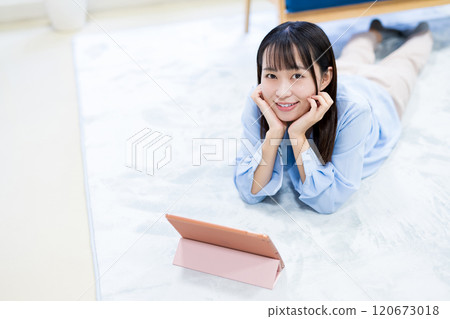 Young woman watching YouTube videos on a tablet while resting her chin on her hands, holiday, relaxing, watching videos 120673018