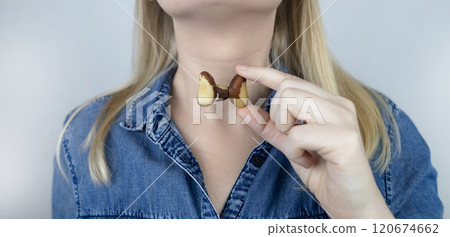 Prevention of thyroid disease. Woman holding a brazil nut in the shape of a thyroid gland. Nut rich in selenium 120674662