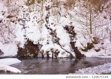 small waterfall in winter forest. ice covered creek. frozen water and leafless trees on the snow covered hillside. remote backcountry 120675144