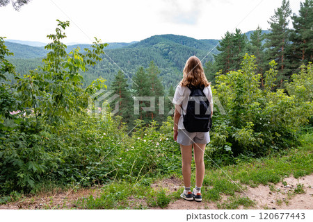 Woman with a backpack enjoying a scenic forest view from a hilltop. Woman with a backpack enjoying a scenic forest view from a hilltop. 120677443