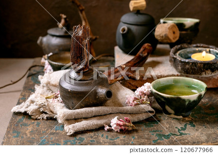 Chinese Tea Ceremony. Three traditional handmade ceramic black teapots with wooden handle on dark wooden table. Ceramic teacups and pink spring flowers, burning tea candle. Tea ceramics 120677966