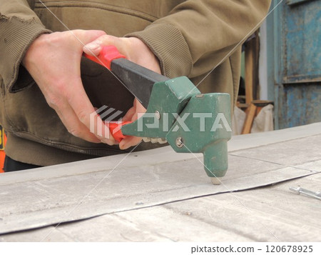 A builder fastens the gray flat metal plates with a green riveting tool.  120678925