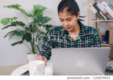 One woman student sitting at home writing and reading in her notebook holding pencil while study preparing for exam learning and education concept real people. 120679055