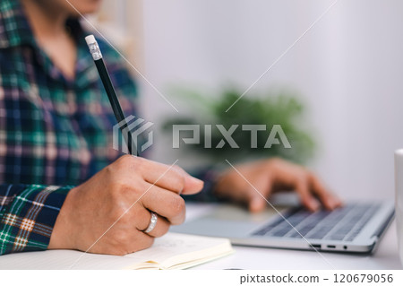 A woman hand holding a pencil while working at small office and using a laptop. Close up shot hands of freelancer use laptop working on desk of her this is a lifestyle of freelance or editor. A woman hand holding a pencil while working at small office and using a laptop. Close up shot hands of freelancer use laptop working on desk of her this is a lifestyle of freelance or editor. 120679056