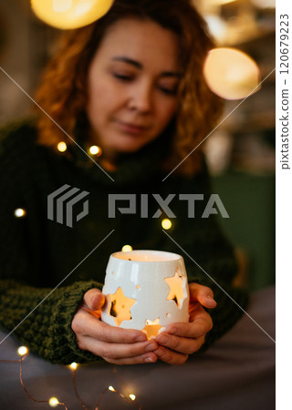 Woman holding a glowing candle lantern with holiday lights, celebrating Christmas and New Year in a serene and festive atmosphere Woman holding a glowing candle lantern with holiday lights, celebrating Christmas and New Year in a serene and festive atmosphere 120679223