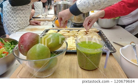 People preparing food sprinkling cheese on something on baking pans, table view on smoothie and mangoes with hands over the food People preparing food sprinkling cheese on something on baking pans, table view on smoothie and mangoes with hands over the food 120679684