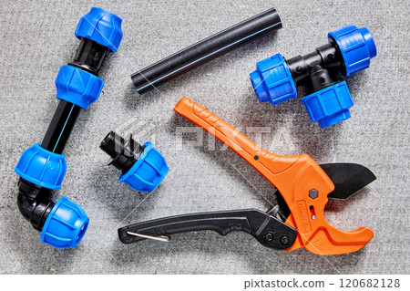 Assembly of outdoor water supply for drinking water and irrigation, compression fittings for plastic pipes laid out on gray surface next to ratchet pipe cutter. Assembly of outdoor water supply for drinking water and irrigation, compression fittings for plastic pipes laid out on gray surface next to ratchet pipe cutter. 120682128