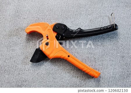 An orange and black pipe cutter lies on concrete surface. 120682130