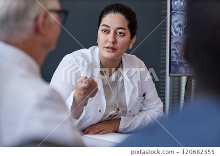 Portrait of Middle Eastern female radiologist talking to colleague collaboratively planning patients treatment in group at meeting in medical office, copy space 120682355