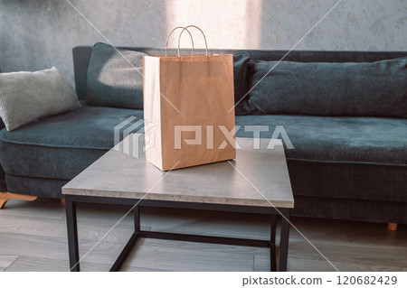 Disposable bag of kraft paper with products left by courier of food delivery service on a table at home. Copy space. Kraft design. Disposable bag of kraft paper with products left by courier of food delivery service on a table at home. Copy space. Kraft design. 120682429