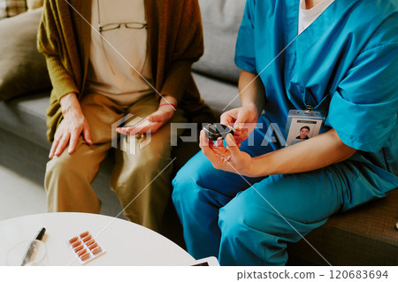 Nurse in blue scrubs giving medication to senior sitting on couch in warm room setting, medical care and support provided to elderly patient for safe drug administration Nurse in blue scrubs giving medication to senior sitting on couch in warm room setting, medical care and support provided to elderly patient for safe drug administration 120683694