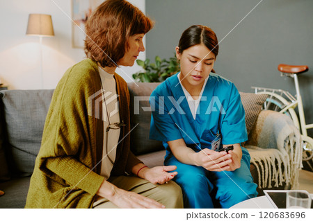 Nurse assisting elderly woman with health checkup in cozy living room setting, medical equipment and caring nurse ensuring proper care for patient in relaxed environment Nurse assisting elderly woman with health checkup in cozy living room setting, medical equipment and caring nurse ensuring proper care for patient in relaxed environment 120683696