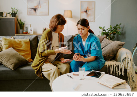 Nurse and patient sitting on couch discussing medical treatment options, with medical tablets, pills, and notes nearby Nurse and patient sitting on couch discussing medical treatment options, with medical tablets, pills, and notes nearby 120683697