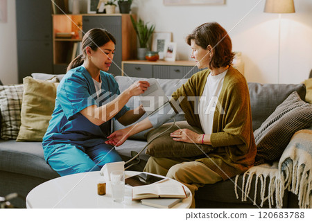 Nurse assisting patient on couch in comfortable home setting, emphasizing compassionate care provided in relaxed environment 120683788