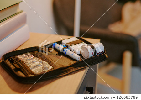 Diabetes medication kit organized on wooden desk with insulin pens, glucose monitor, and necessary supplies in compact case beside books and furniture 120683789