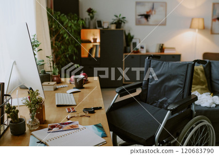 Cozy home office setup combining functional and aesthetic elements with wheelchair near desk, filled with greenery providing inviting workspace and natural lighting enhancing the atmosphere Cozy home office setup combining functional and aesthetic elements with wheelchair near desk, filled with greenery providing inviting workspace and natural lighting enhancing the atmosphere 120683790