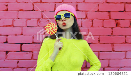 Portrait of stylish modern young woman with lollipop in vivid yellow sweater, glasses, pink hat 120684851
