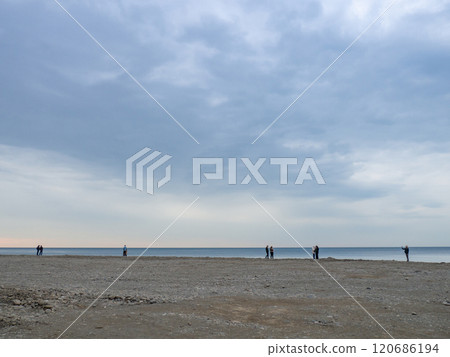 Small silhouettes of people on the shore. People in the distance stand and look at the sea. Overcast weather. Out of season at the Small silhouettes of people on the shore. People in the distance stand and look at the sea. Overcast weather. Out of season at the 120686194