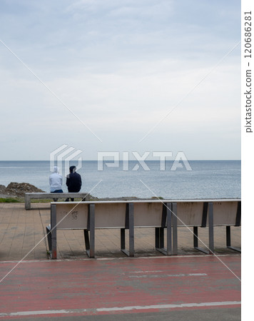 A couple is sitting on a bench by the sea. Cloudy weather at the resort. Not the season for tourism. Recreation of people on the coast. A couple is sitting on a bench by the sea. Cloudy weather at the resort. Not the season for tourism. Recreation of people on the coast. 120686281