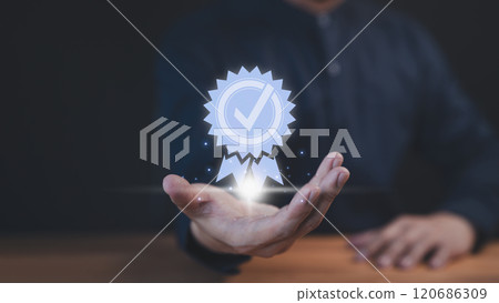 A businessman holds a glowing digital certification badge with a checkmark symbol, representing quality, trust, and achievement. The futuristic design highlights success and recognition. 120686309