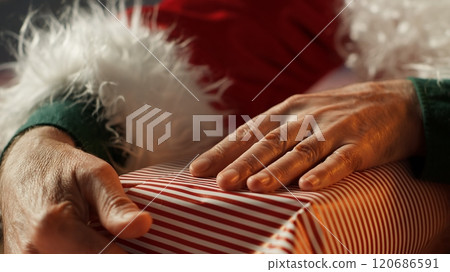 Saint Nicholas decorates a festive present box in his North Pole workshop, preparing wrapped gifts for children on Christmas eve. Colorful ornaments fill the holiday with magic. Close up. Camera A. 120686591