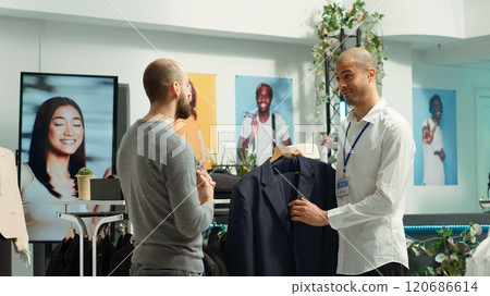 Middle eastern employee assisting client to choose from the new collection of items, presenting higher fabric quality and potential color assortments. Professional retail experience. Camera A. Middle eastern employee assisting client to choose from the new collection of items, presenting higher fabric quality and potential color assortments. Professional retail experience. Camera A. 120686614
