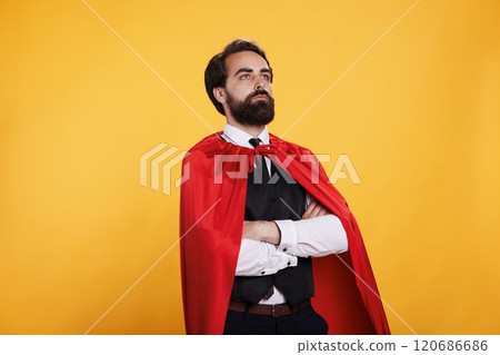 Powerful fantasy hero with red mantle standing against blue background, feeling determined and strong in studio. Young dedicated man acting like a superhero or superhuman, leader inspiration. 120686686