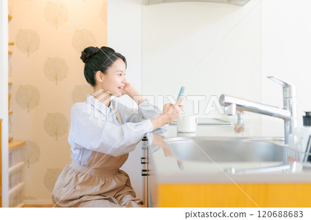 觀看一個智能手機的婦女在廚房裡 120688683