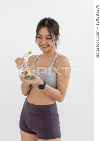 Asian attractive lady sportswear healthy eating salad vegetables over white background. Female holding salad bowl various vegetables and fruit healthy food for weight loss and exercise. 120691270
