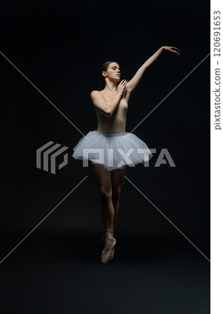 Graceful ballet dancer performing an elegant pose in a dimly lit studio Graceful ballet dancer performing an elegant pose in a dimly lit studio 120691653